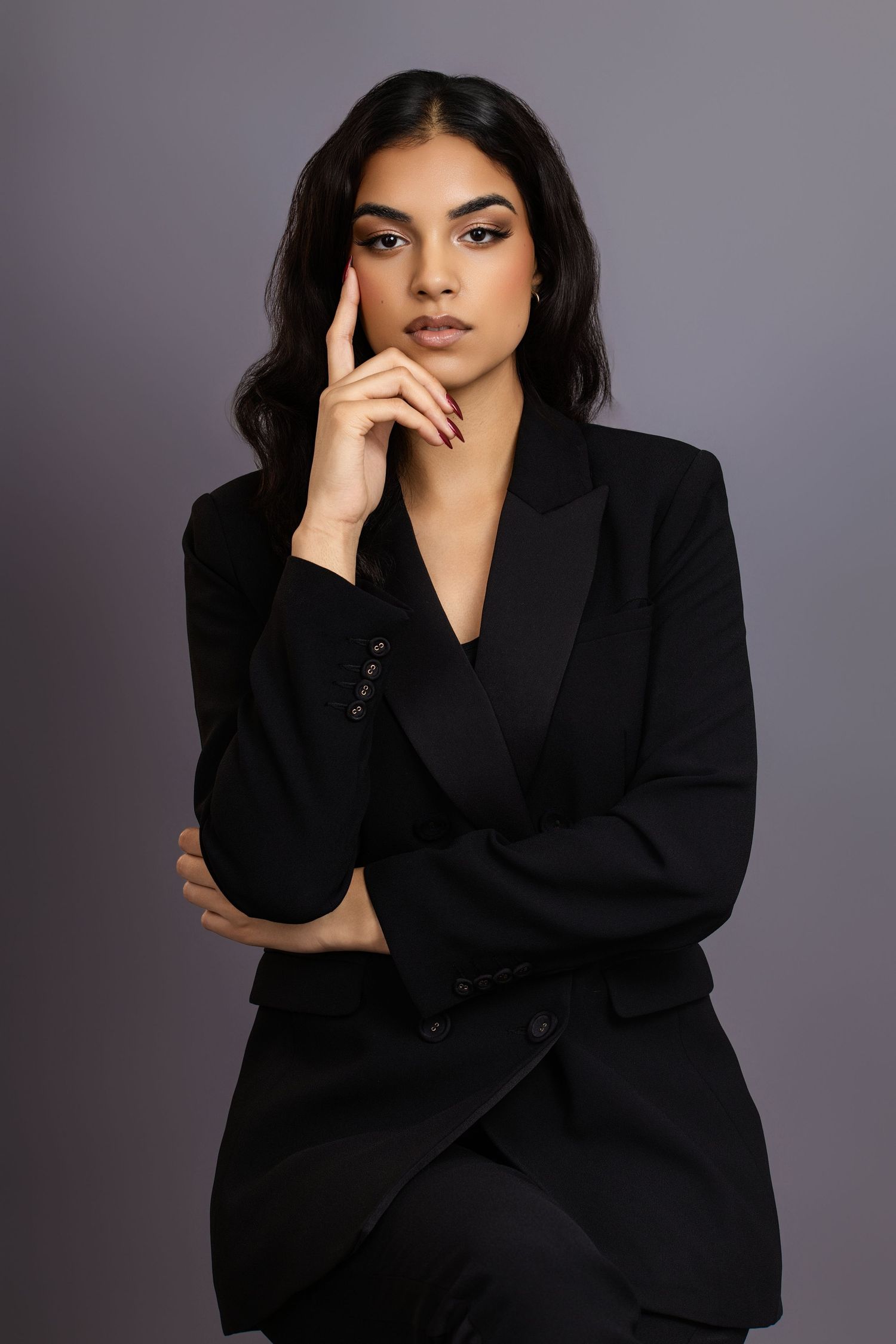 Professional studio portrait of a woman in a black blazer against a gray background.