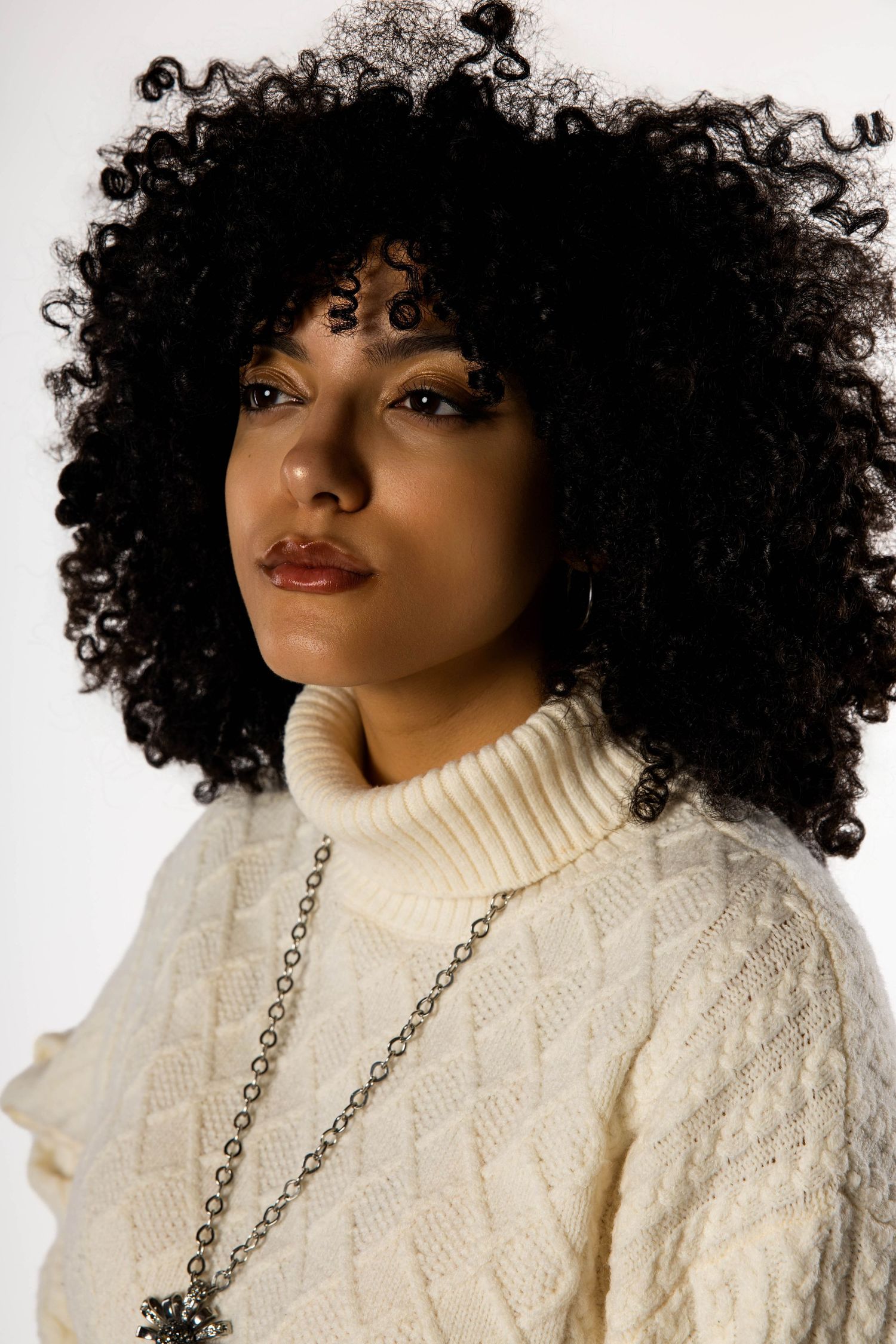 Portrait in cream cable knit sweater with natural curly hair against white background.