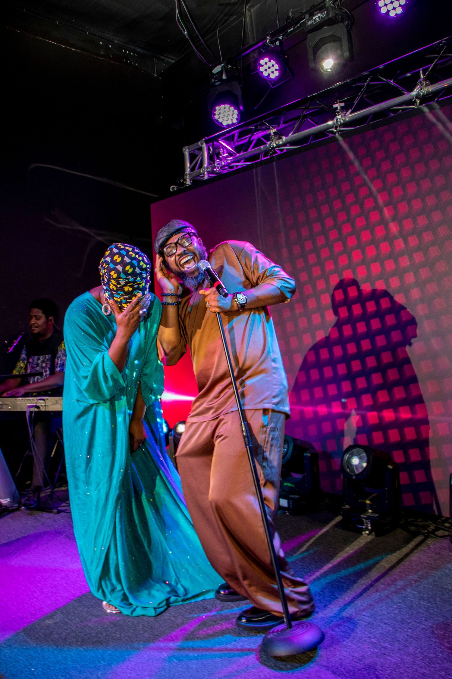 Musicians performing energetically on stage with vibrant purple and red lighting effects.