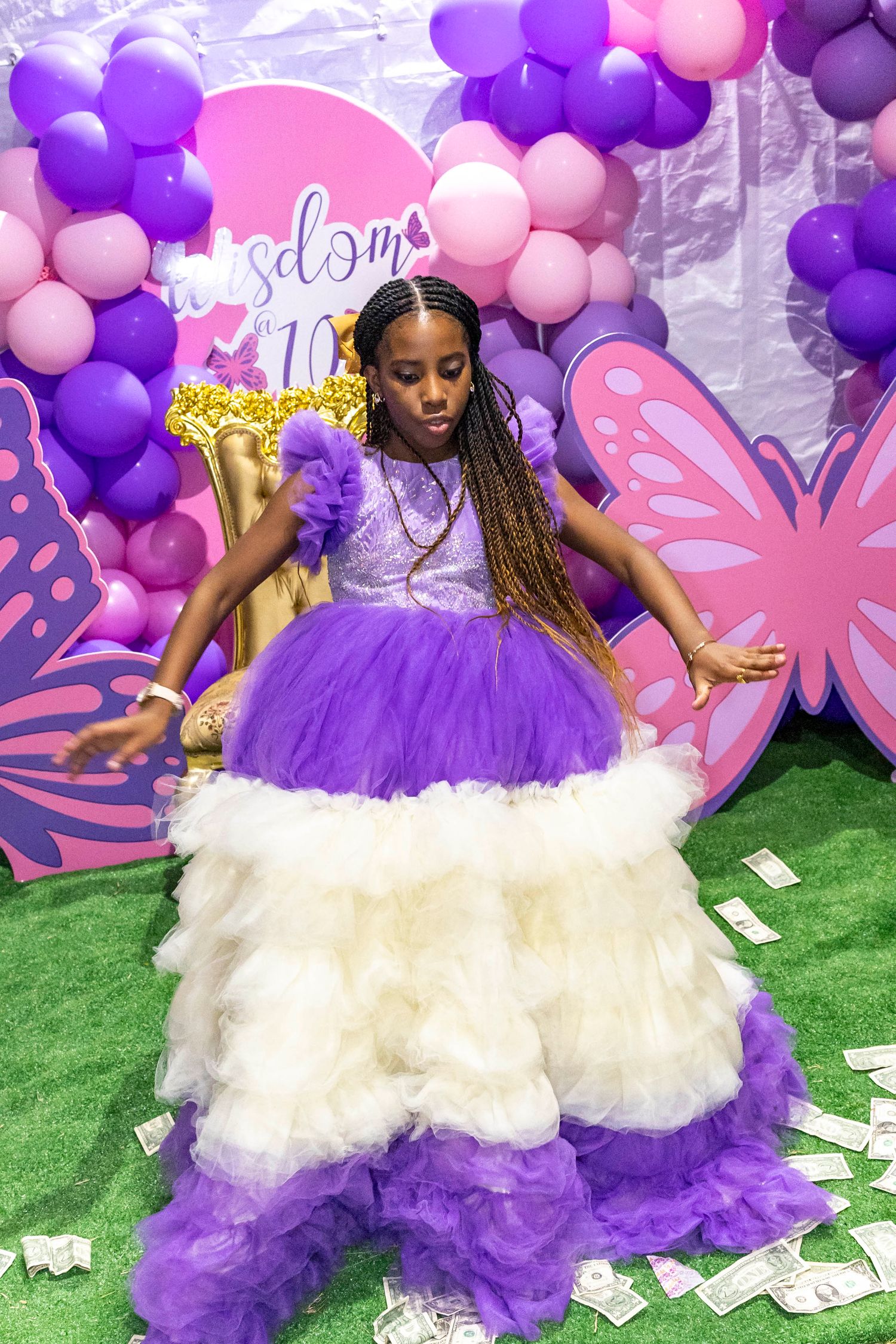 Child wearing a purple and white tulle dress poses playfully with balloons and decorations.