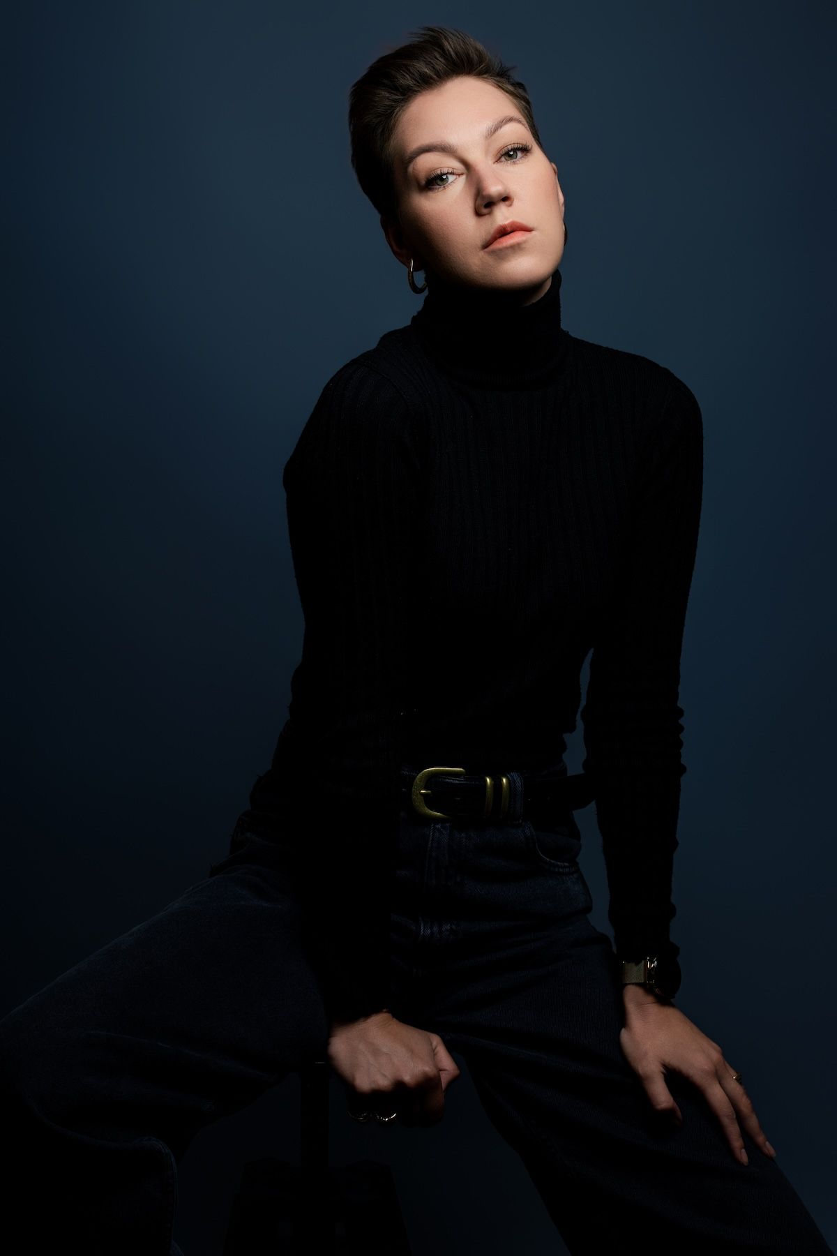 Dramatic fashion portrait series against dark blue backdrop showing model in black attire striking different elegant poses.