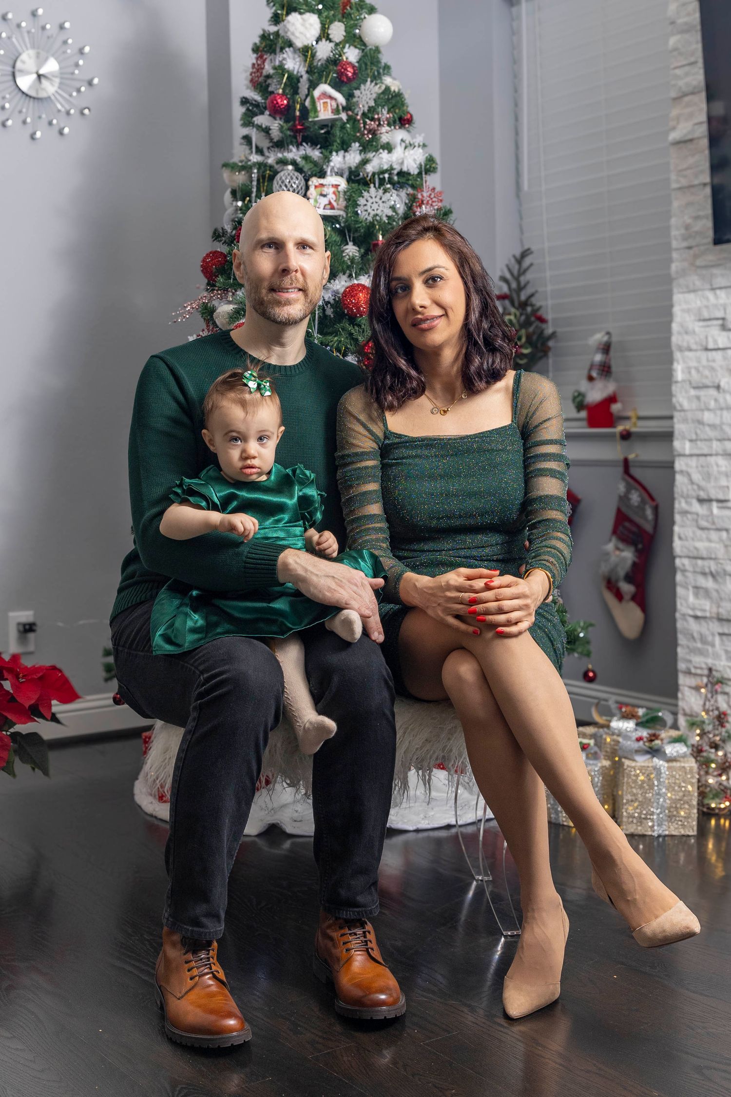 Couple with baby posing by Christmas tree in elegant green and black outfits.