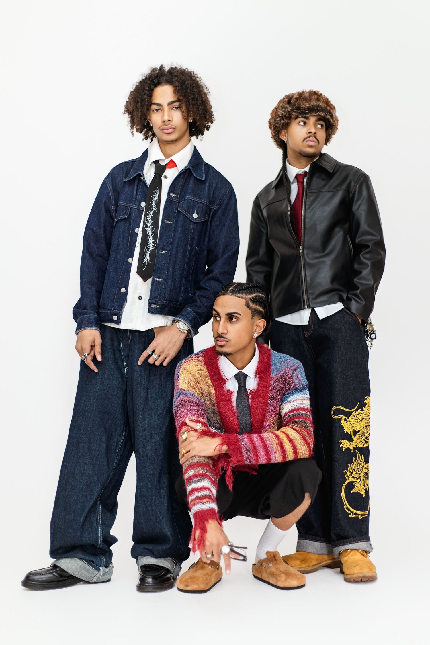Three young models pose in denim and leather jackets with red ties for a fashion photoshoot series.