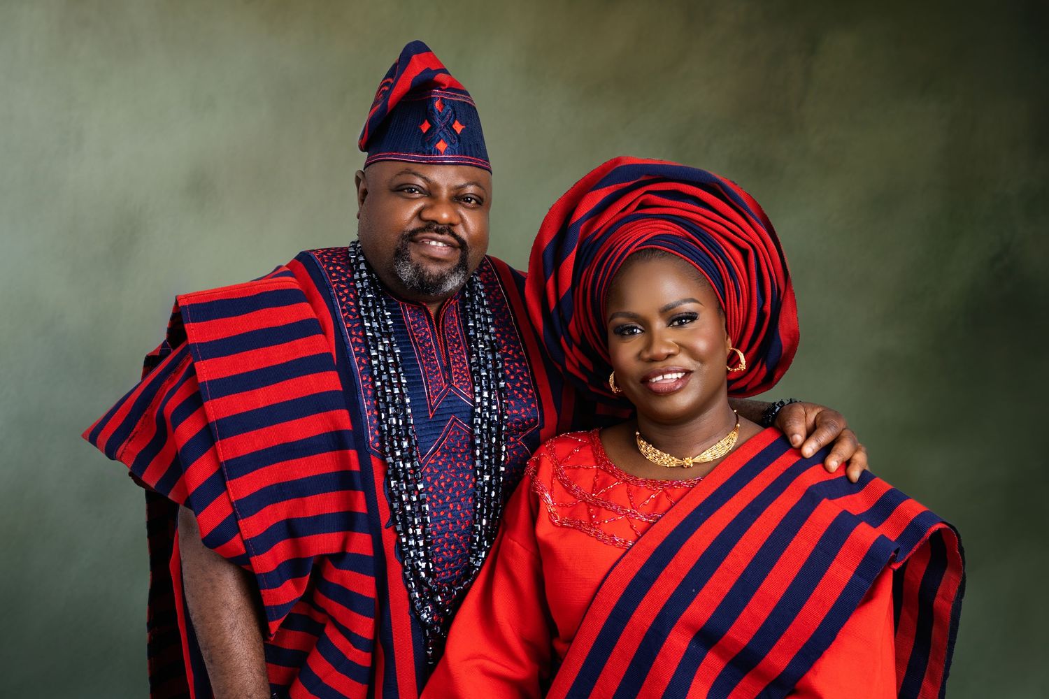 Couple wearing traditional red and blue striped Nigerian attire in studio setting.