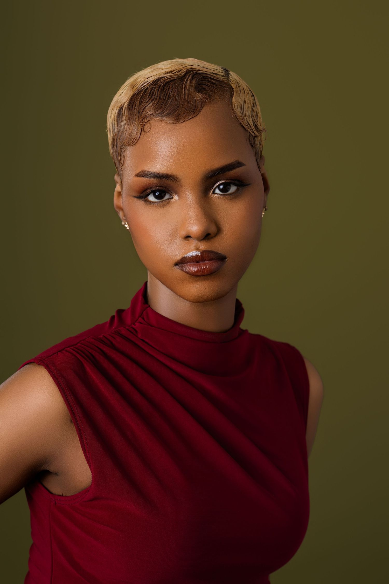 Studio portrait in burgundy sleeveless top against olive green background.