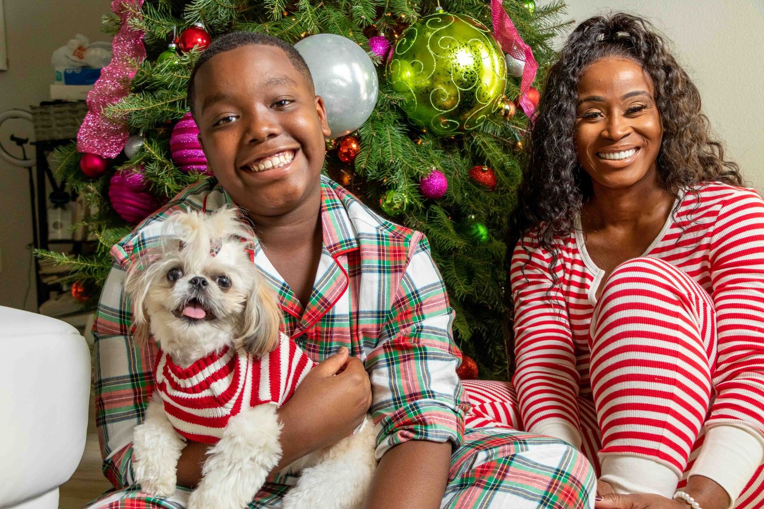 Happy family poses with their dog near decorated Christmas tree with colorful ornaments.