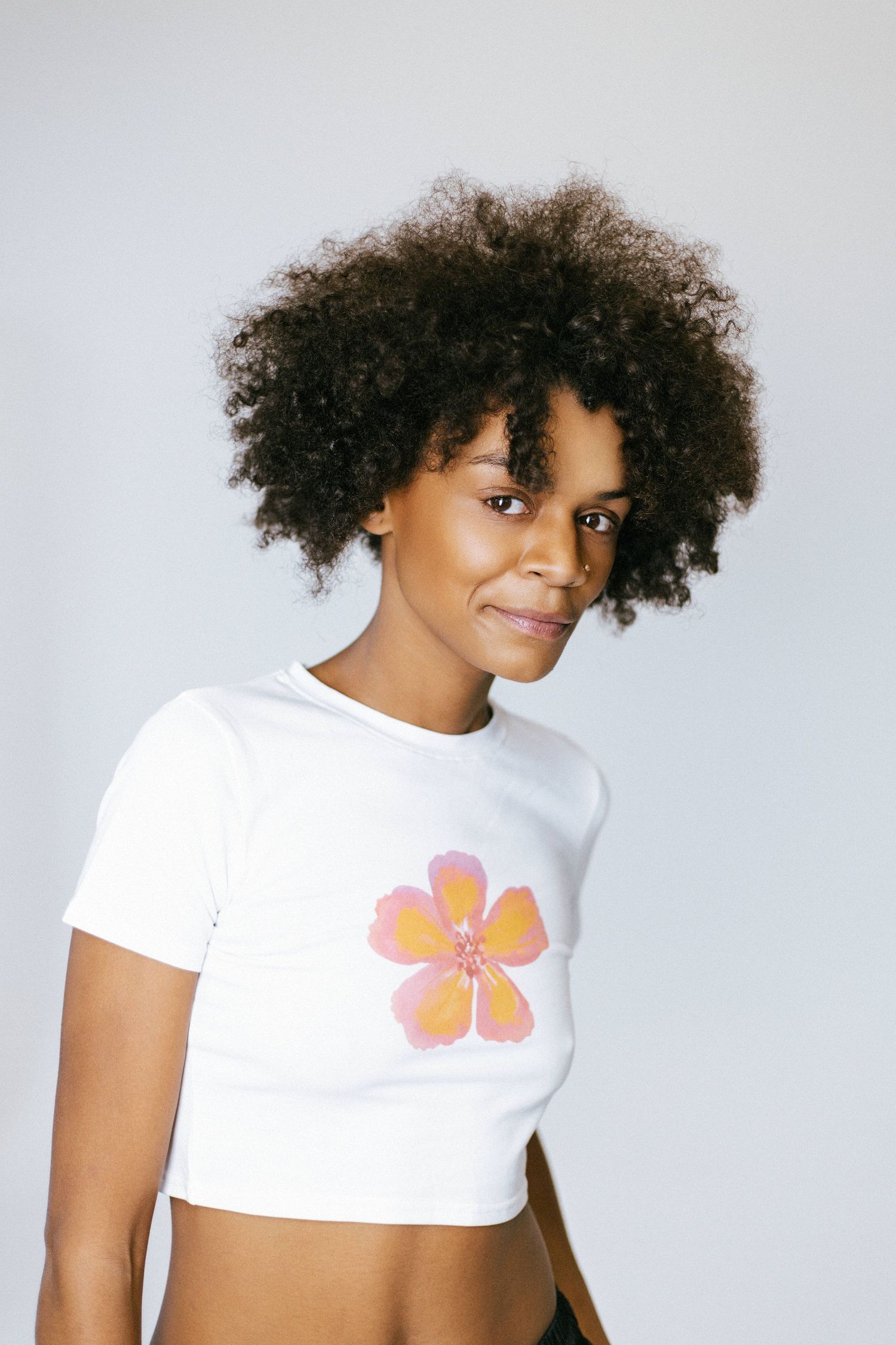 Person with natural curly hair poses in a white t-shirt with a butterfly design against a light background.
