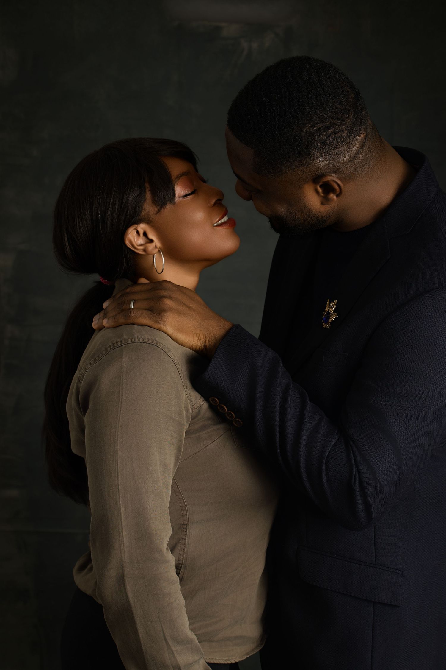 A romantic couple embraces in dramatic lighting against a dark background.