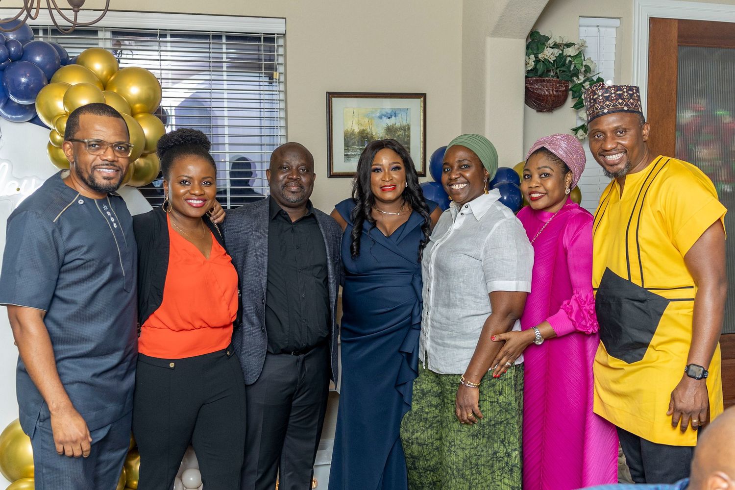 Large group photo of party guests in colorful formal attire at an indoor venue.