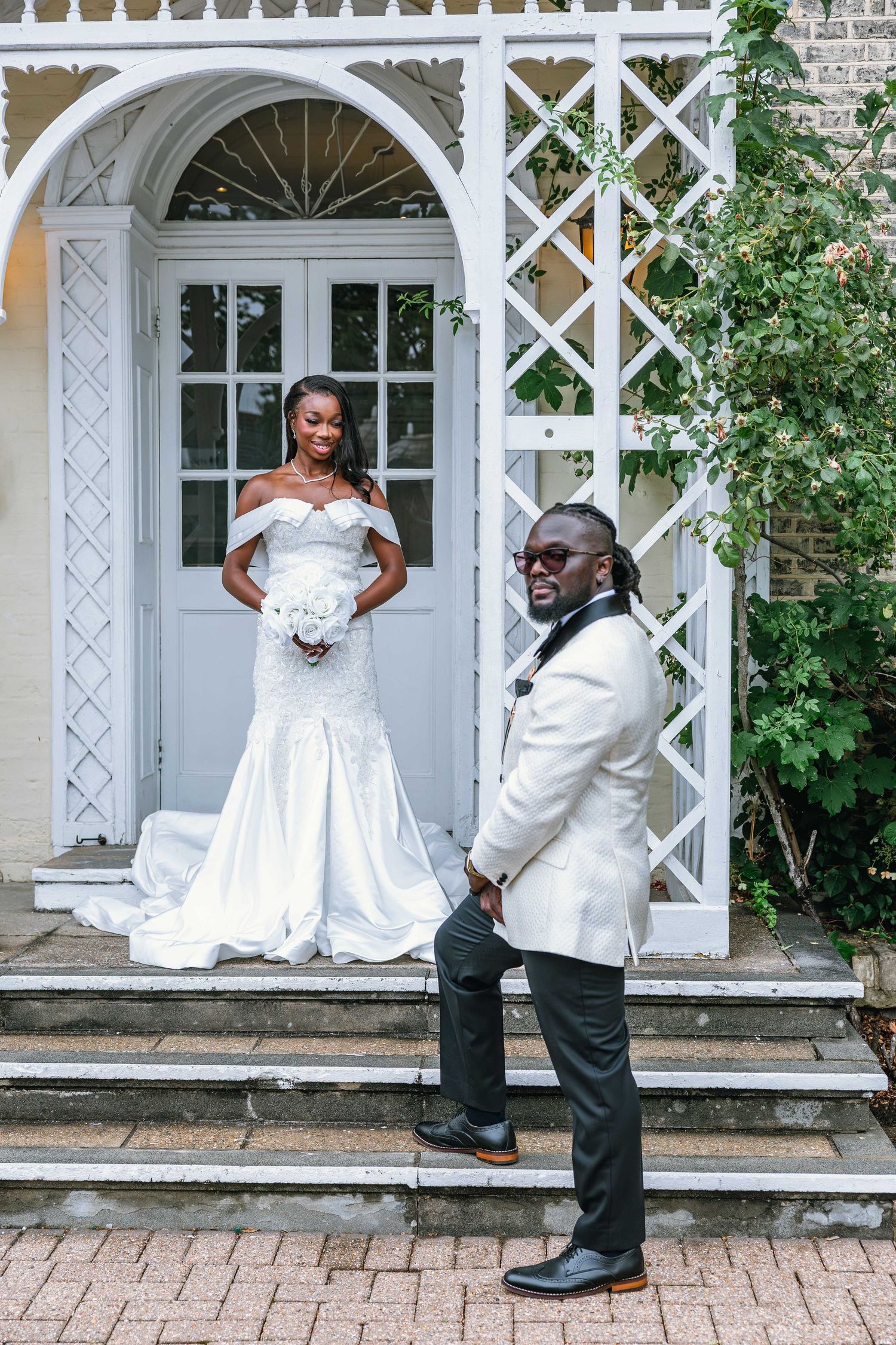 Bride and groom taking playful photos on white porch with lattice details.