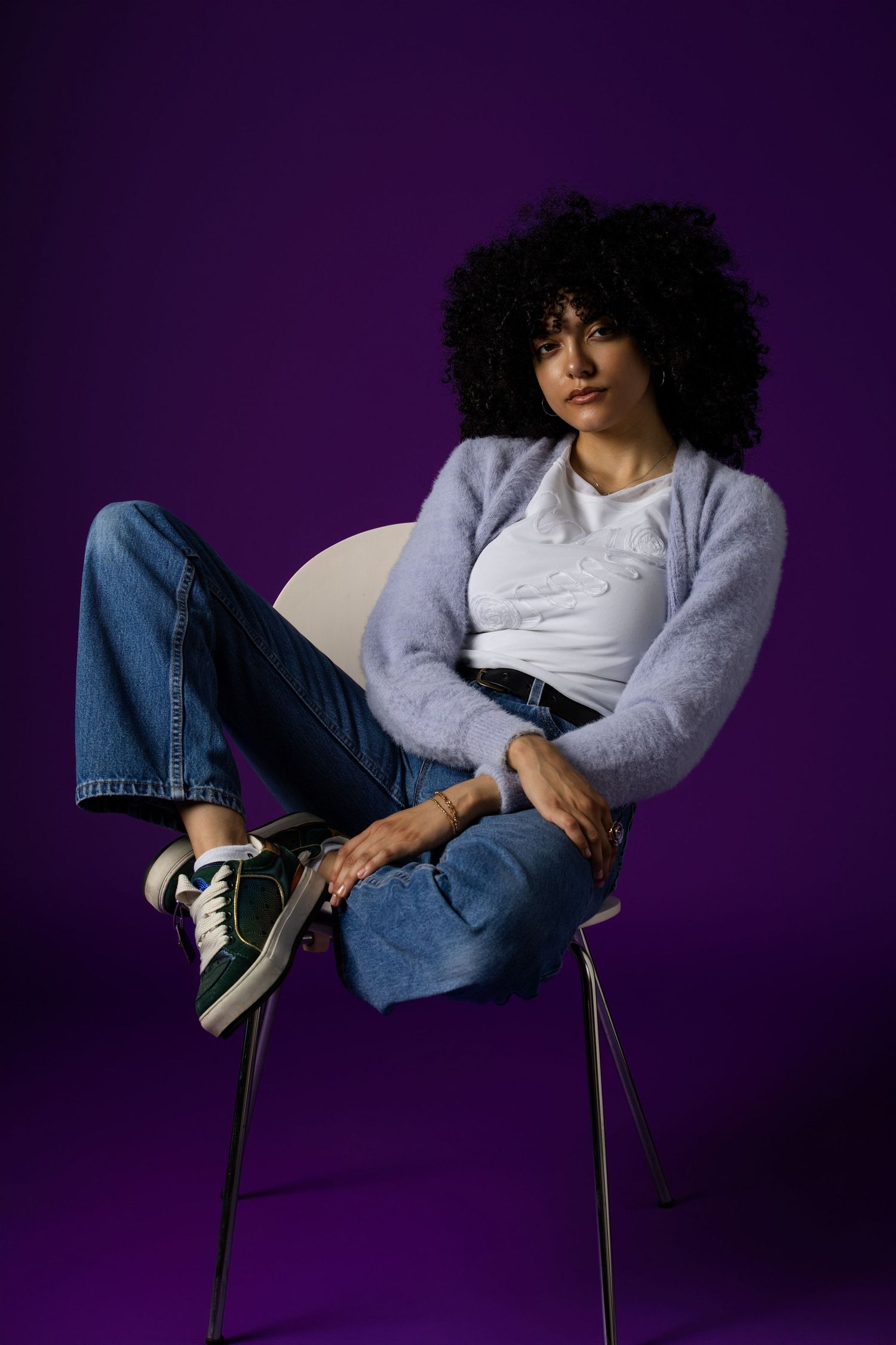 Casual denim and grey sweater look photographed against deep purple background.