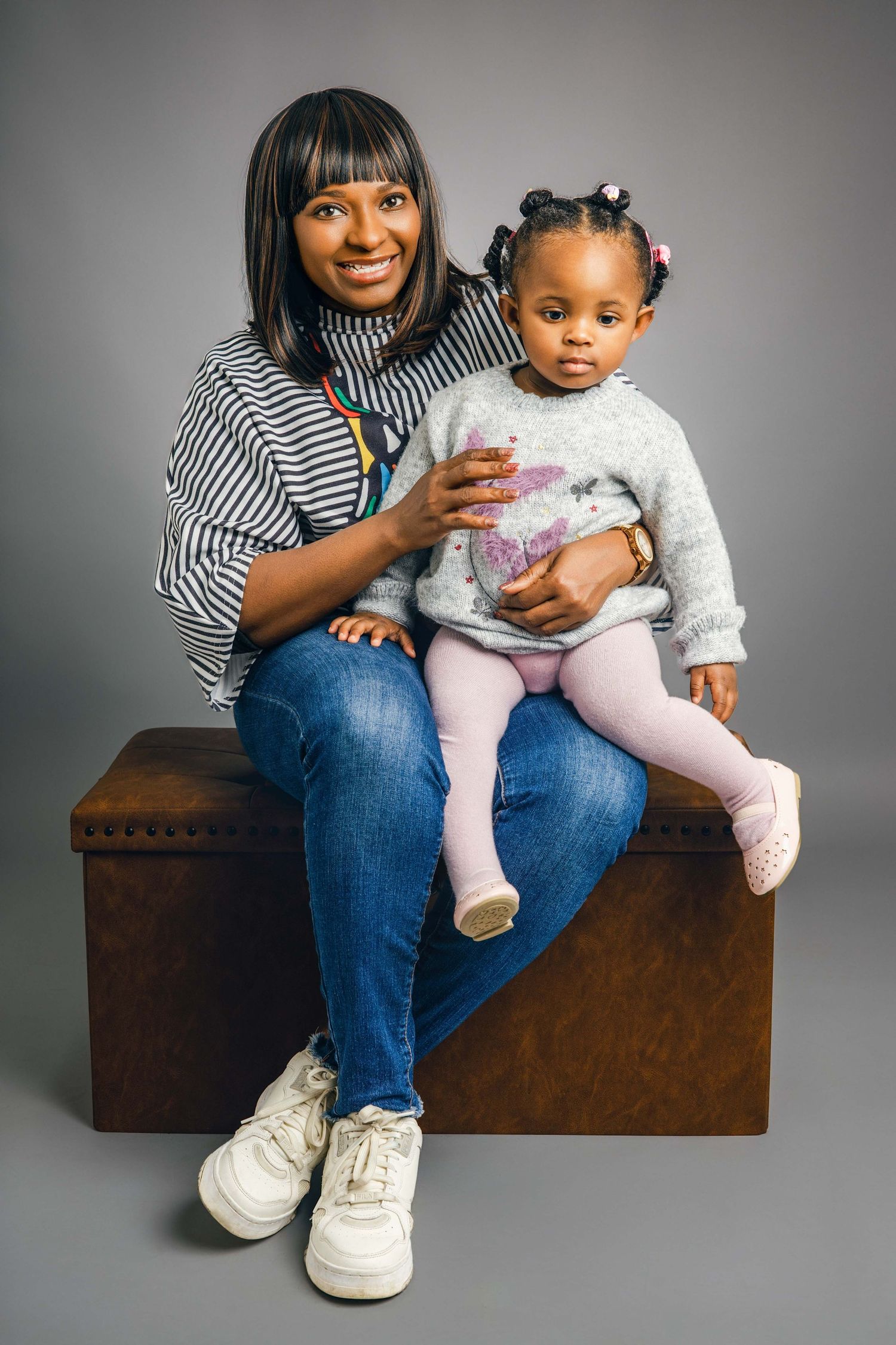 Mother and child sitting on wooden bench during studio photoshoot.