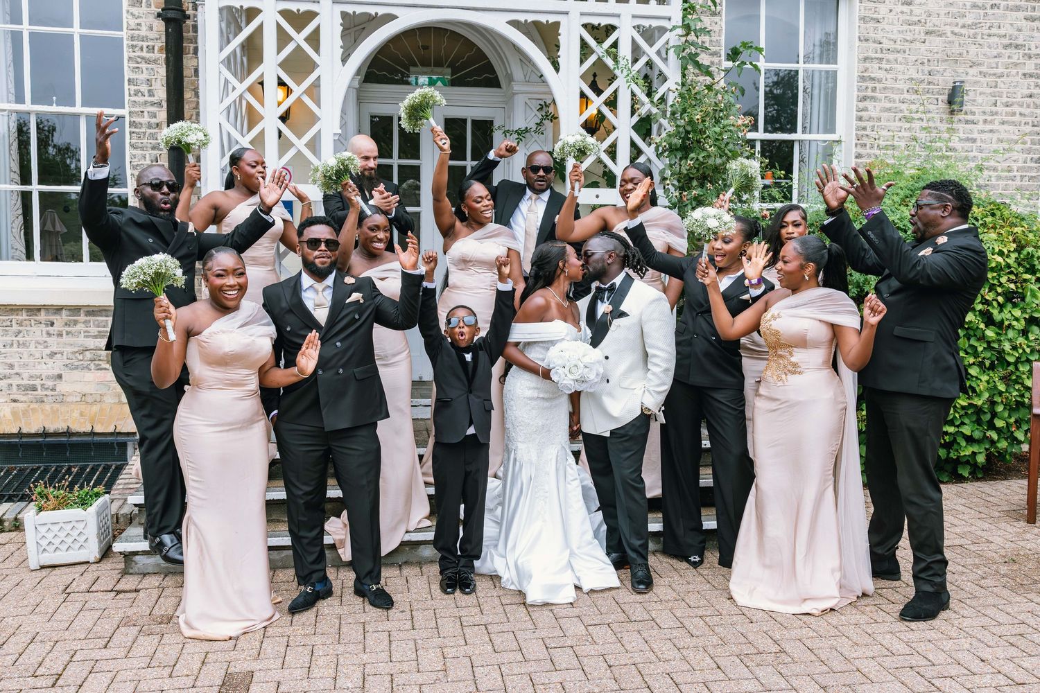 Wedding party group photo in front of elegant stone building with arched windows.