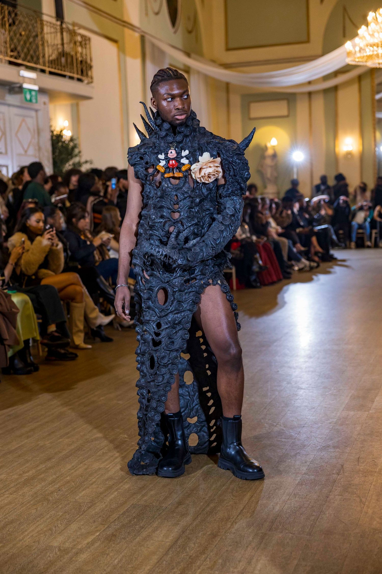 Avant-garde black textured ensemble being showcased on wooden runway at fashion event.
