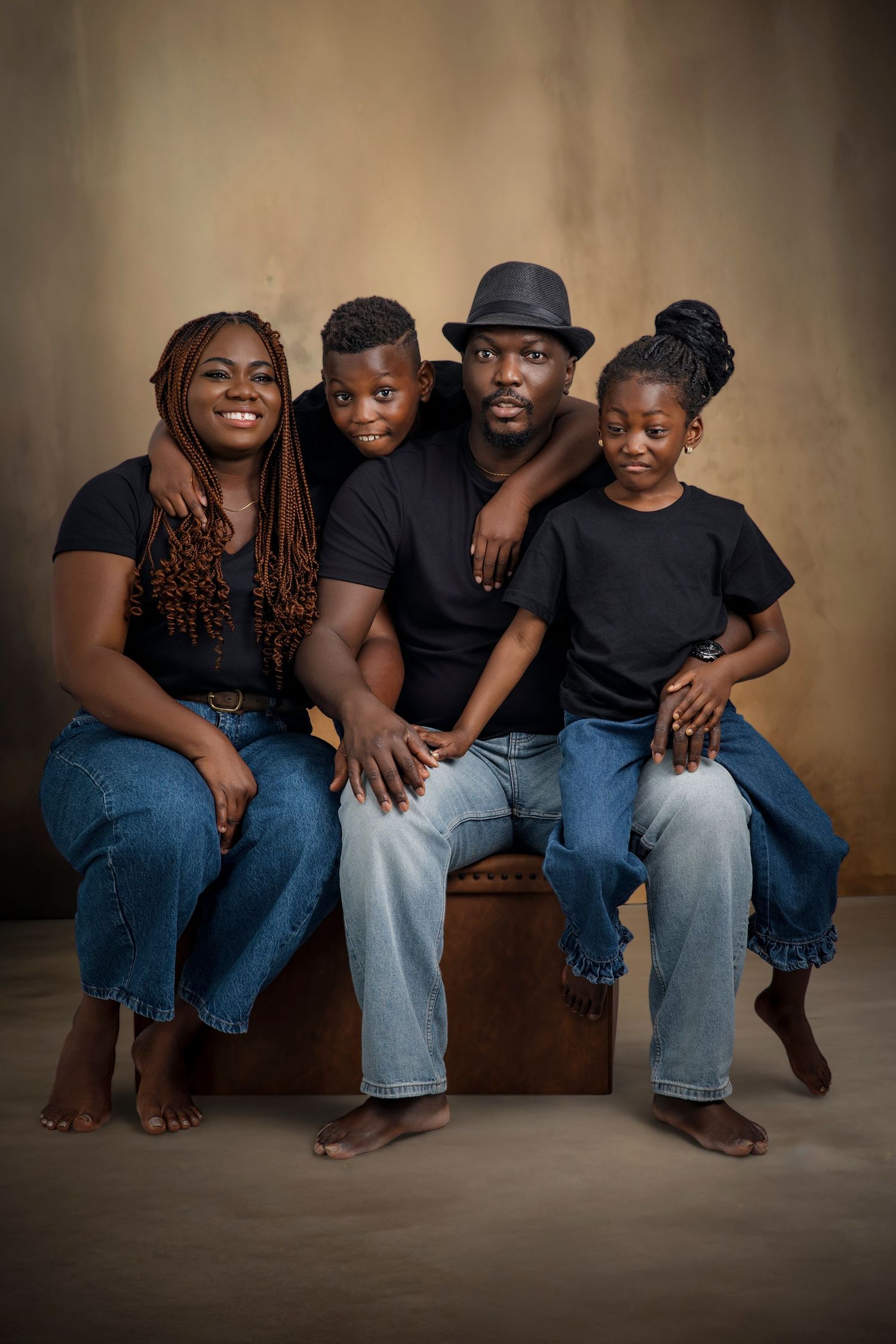 A family sits together on a wooden bench wearing coordinated outfits of black shirts and blue jeans.