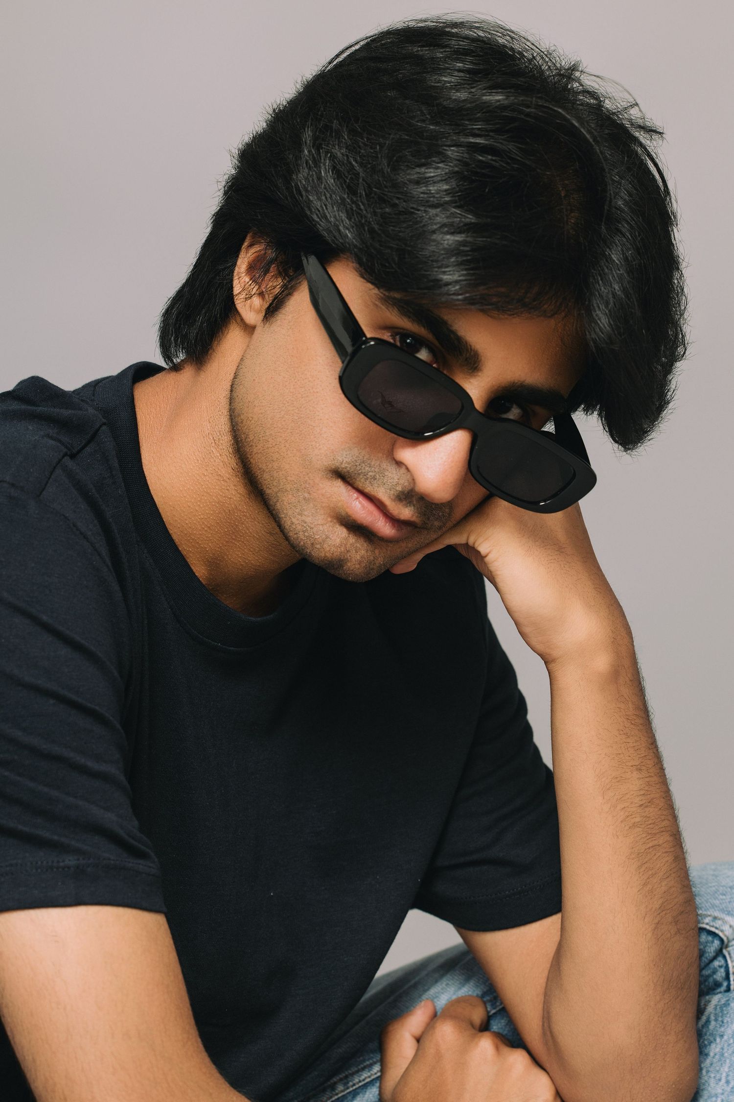 Casual portrait of young person in black t-shirt wearing sunglasses against light background.