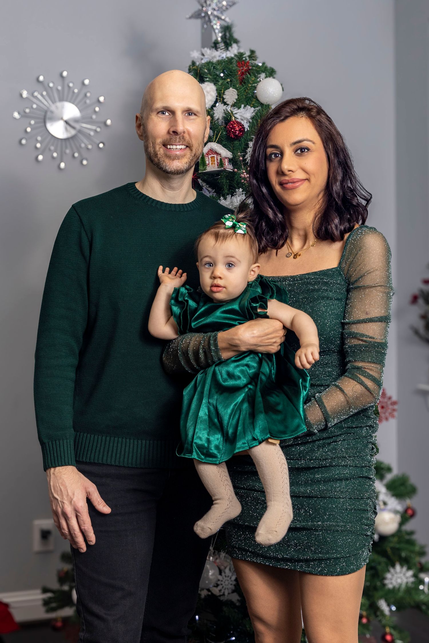 Holiday family portrait with parents and baby in green formal wear by Christmas tree.