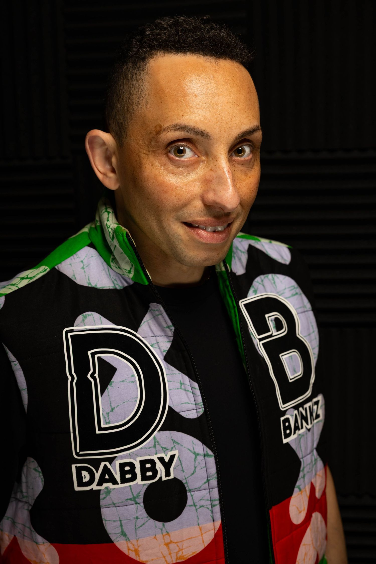 Portrait wearing a black and white Dabby branded shirt against dark background.