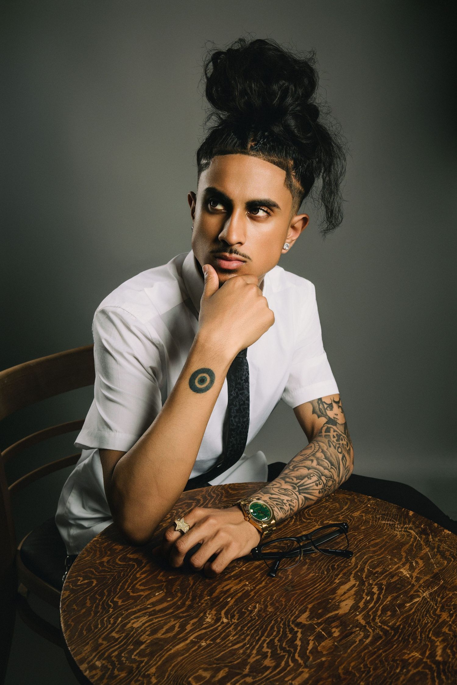 Artistic portrait showing person in white shirt leaning over wooden table in moody lighting.