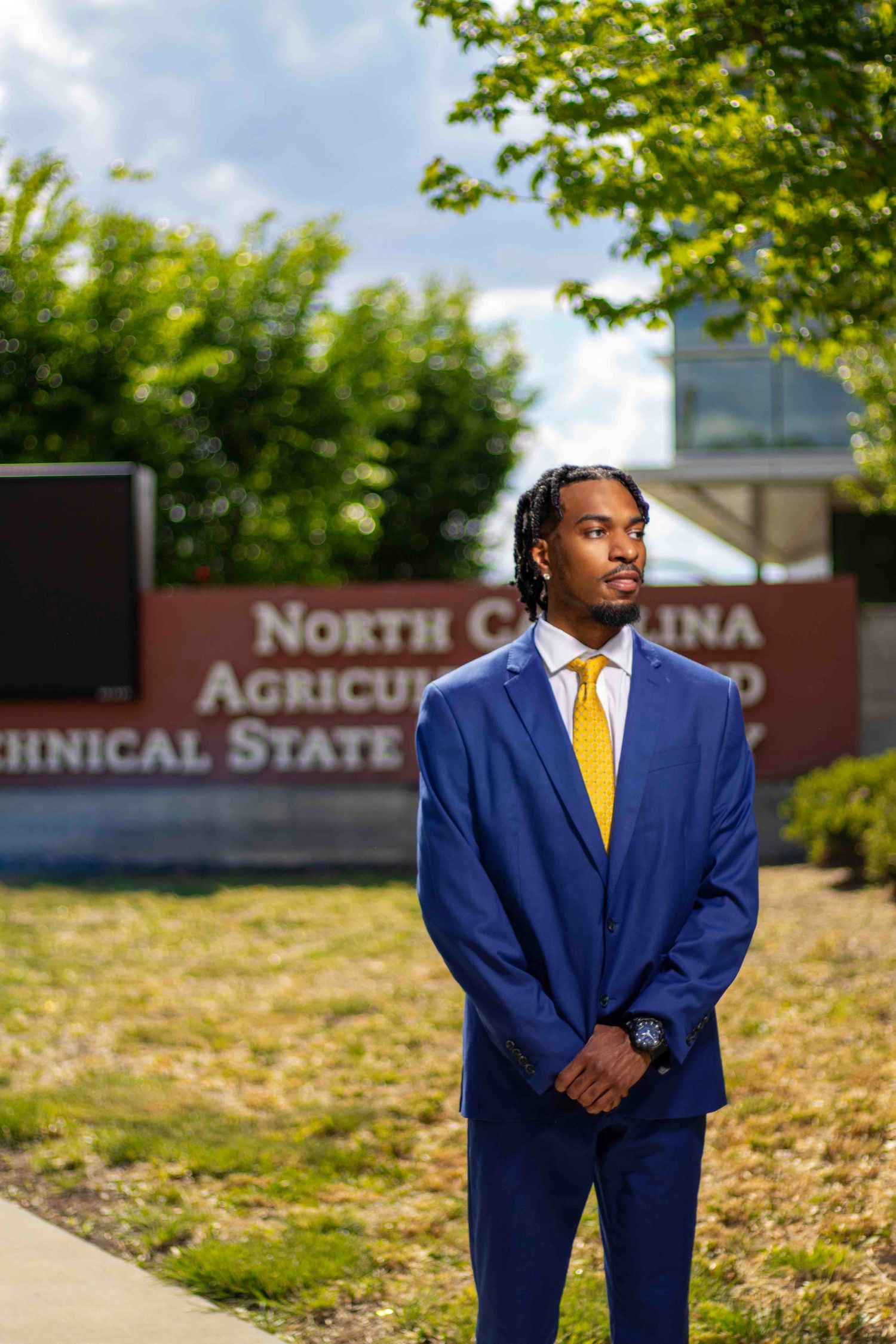 Young man in blue suit and gold tie stands before North Carolina Agricultural and Technical State University sign.