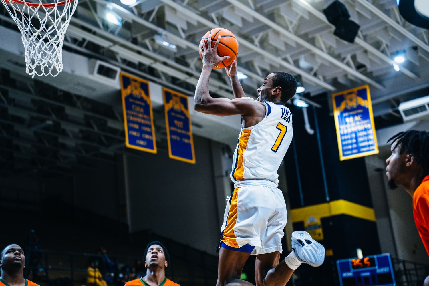 Basketball player in white jersey driving to the hoop for a layup during an indoor arena game.
