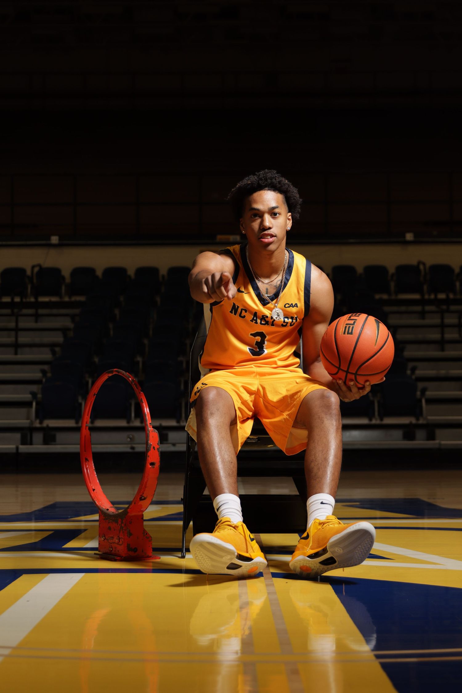 NC A&T basketball player #3 poses with a ball on court in gold uniform.