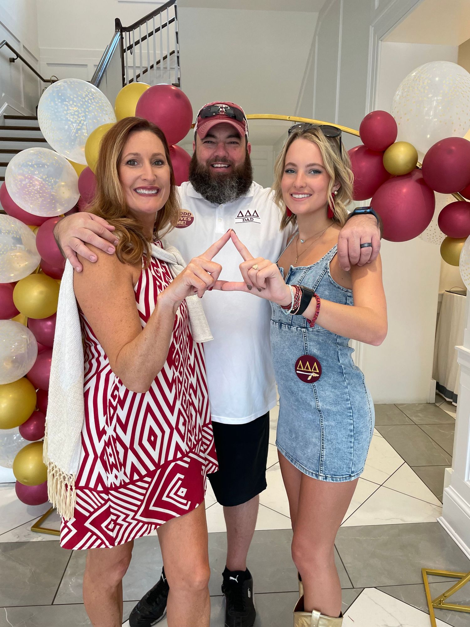 Three people posing together making triangle hand signs at a Delta Delta Delta sorority event with balloon decorations.