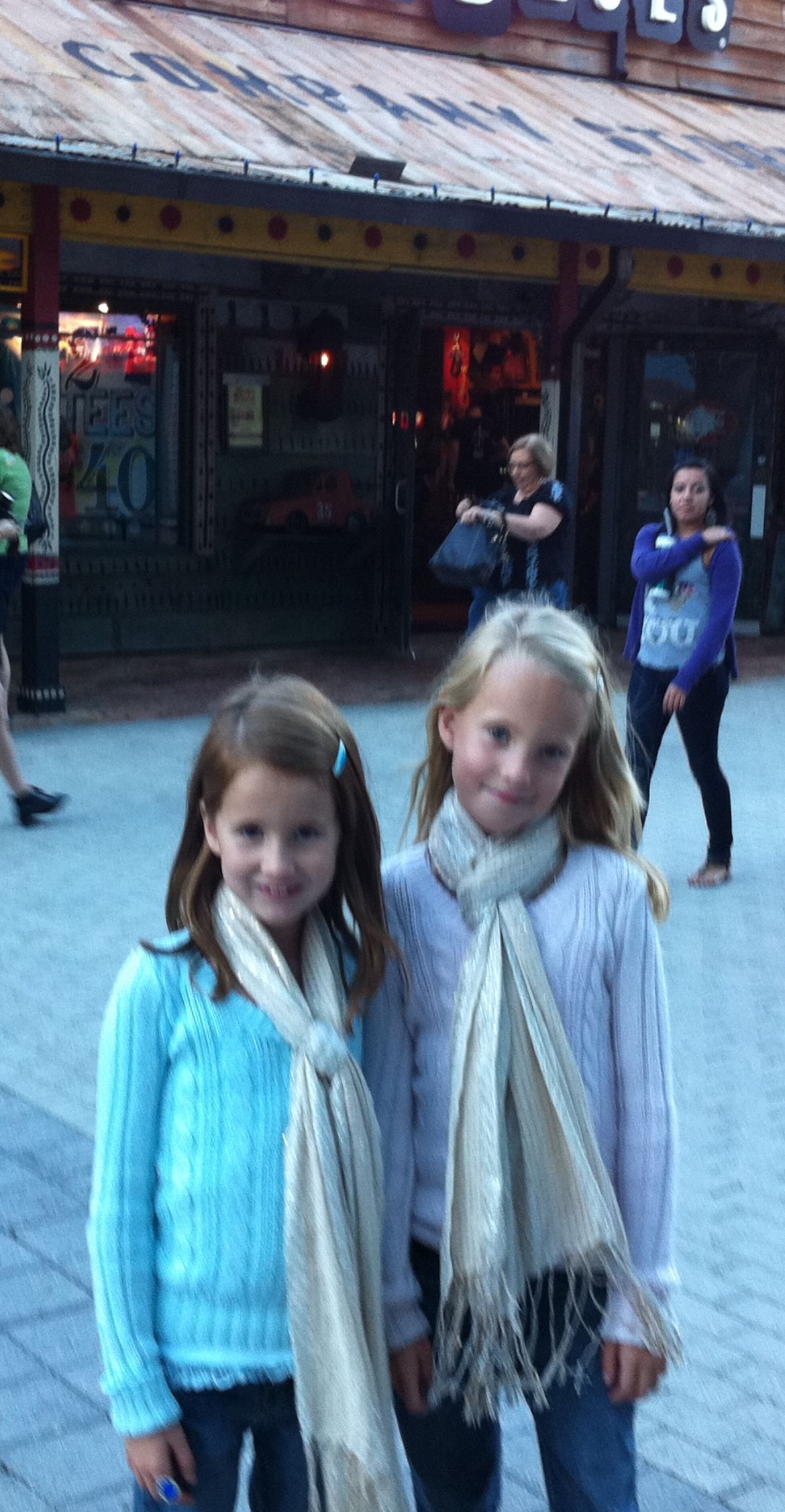 Young girls in winter scarves smiling and posing together at an indoor venue.