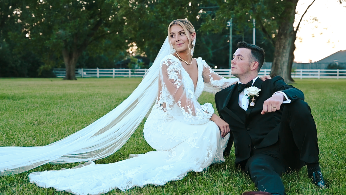 Newlyweds share romantic moment on lawn with bride's veil flowing in breeze.