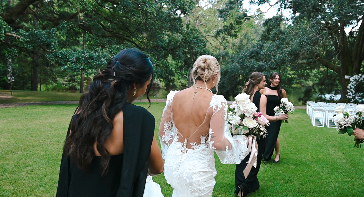 Wedding party walks together across green lawn during outdoor celebration.