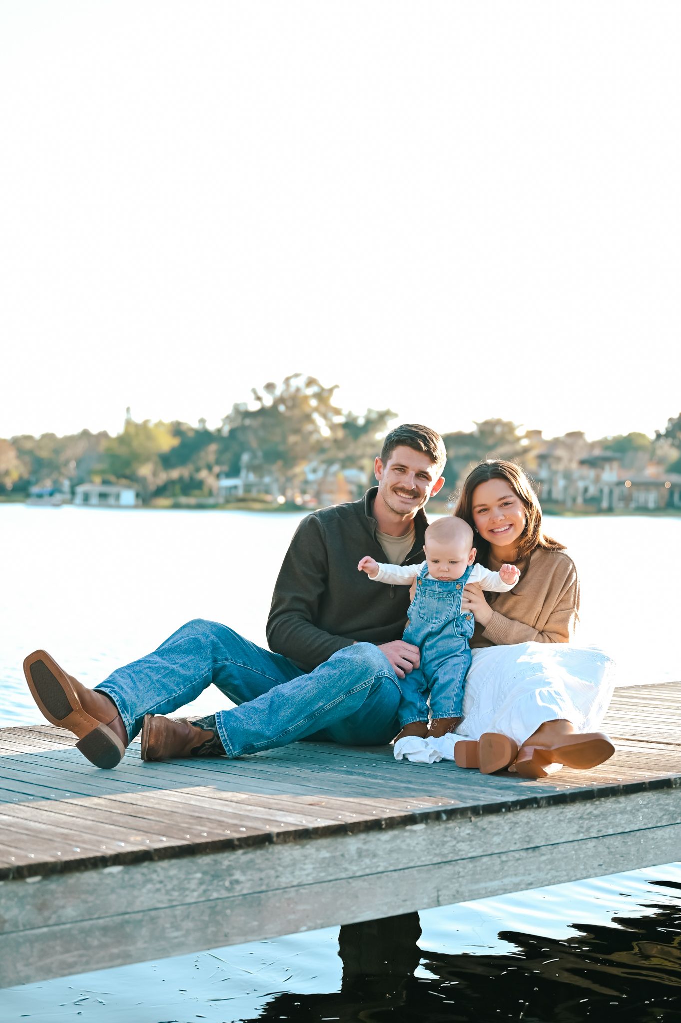 Family relaxing together on a wooden dock by the water during sunset.