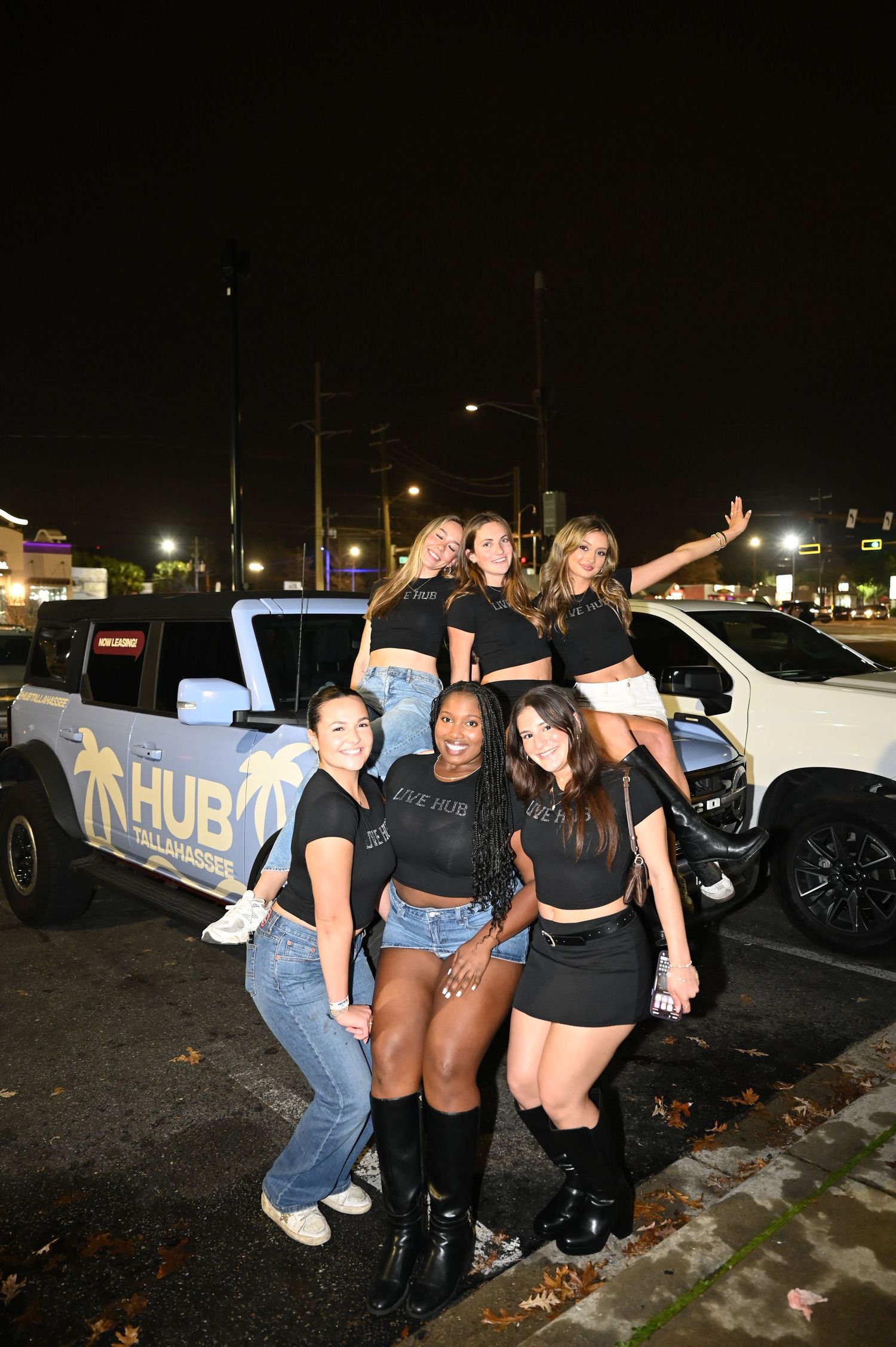 Group of six women posing in front of a white HUB branded truck in a parking lot at night.