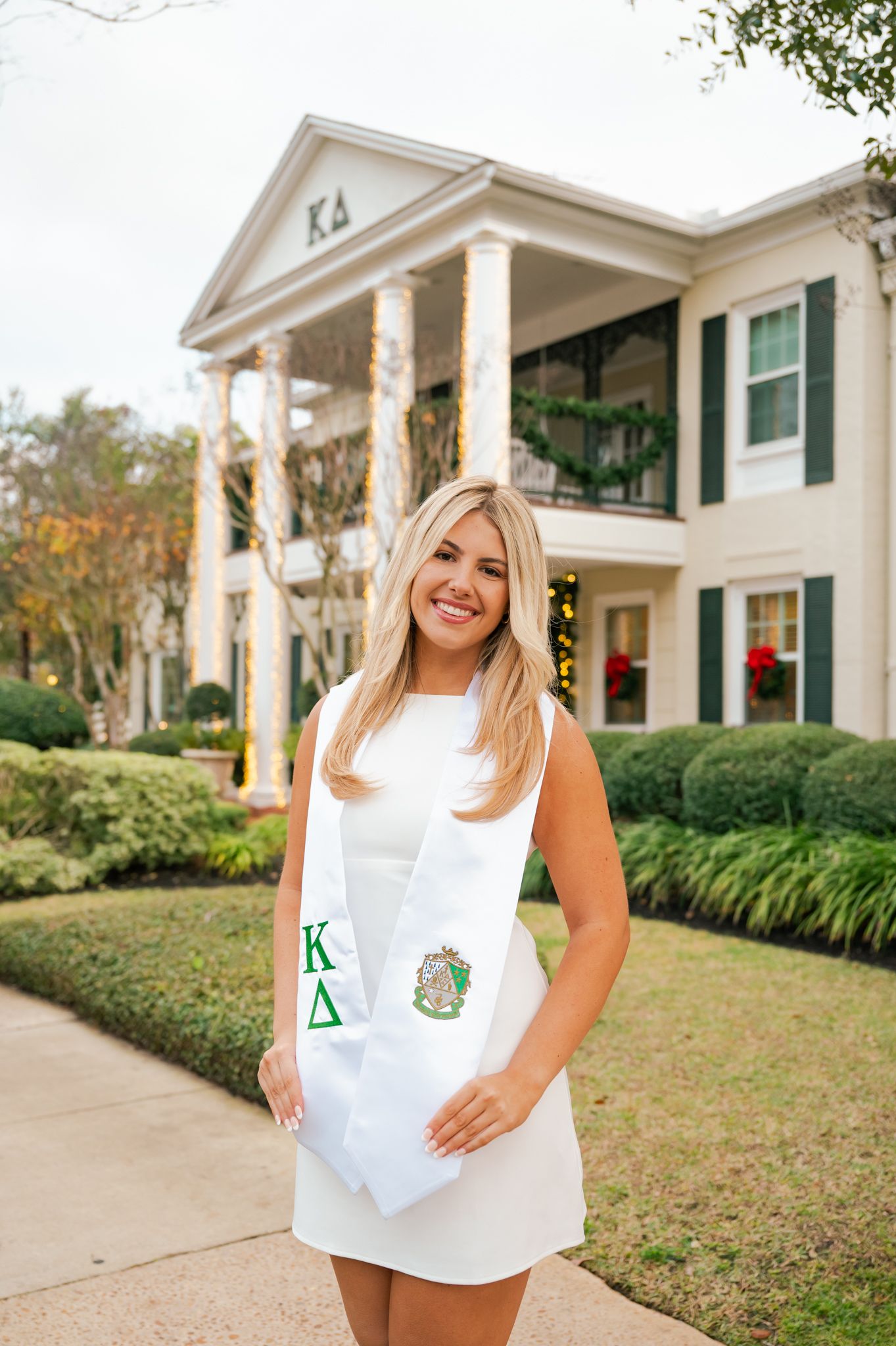 Woman wearing white sorority shirt poses in front of traditional white columned building.