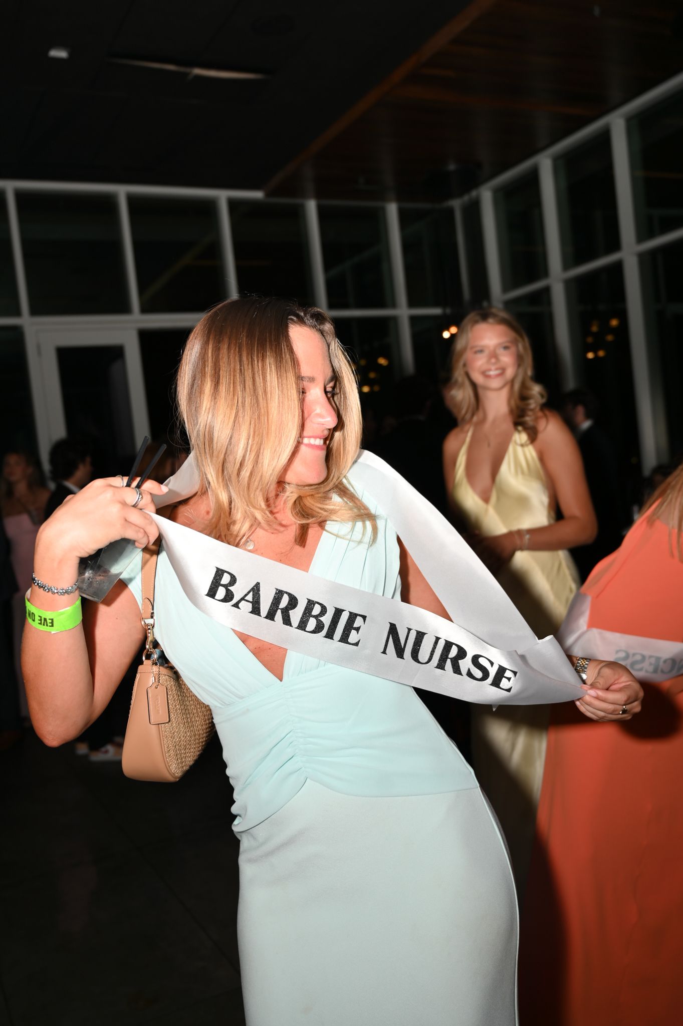 Woman wearing a Barbie Nurse sash at a formal event in a light blue gown, smiling and posing for the camera.