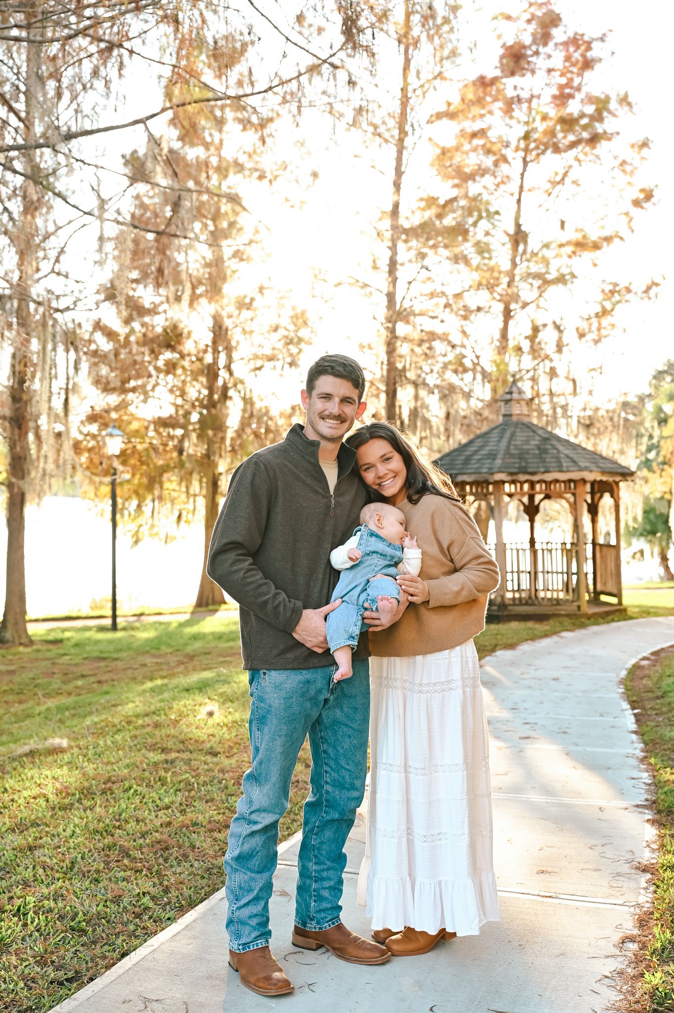 A family poses together in a wooded outdoor setting during golden hour.