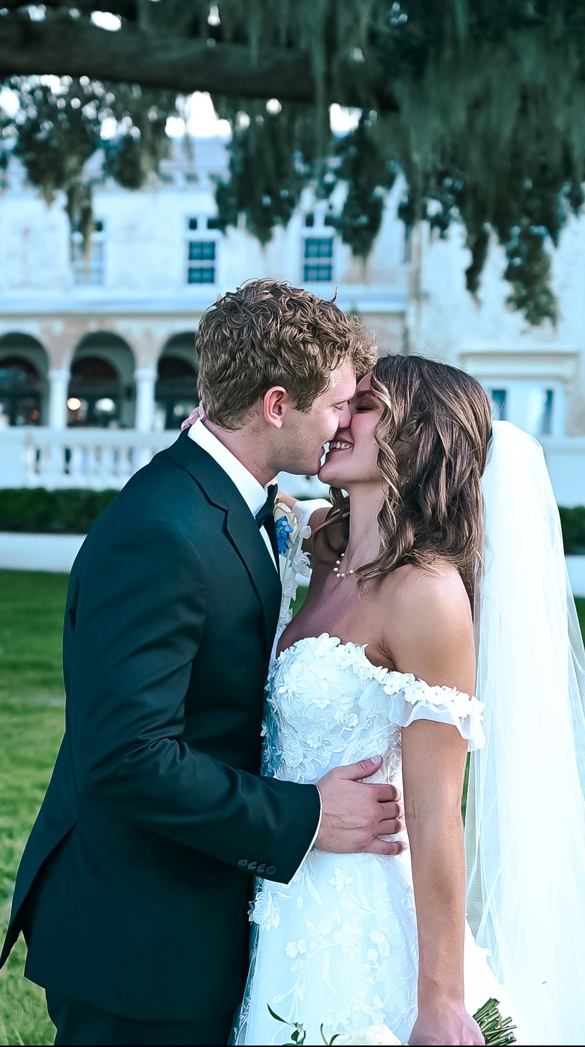 A romantic wedding photo series showing a couple sharing their first kiss as newlyweds in an outdoor garden setting.