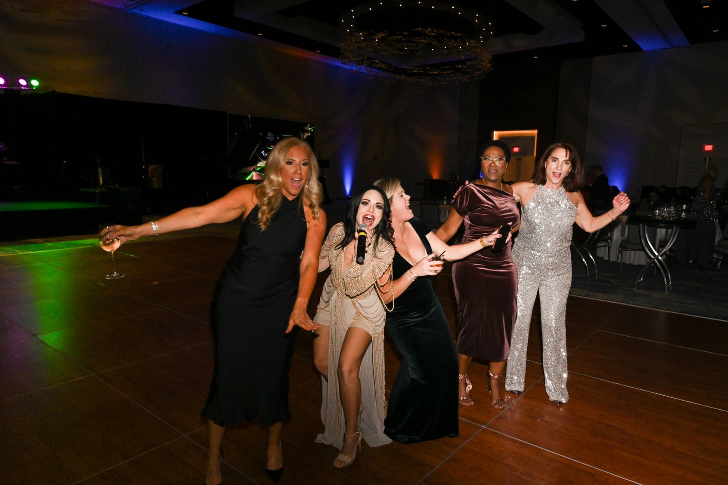 Four women posing and dancing at an elegant formal event in a dimly lit ballroom.