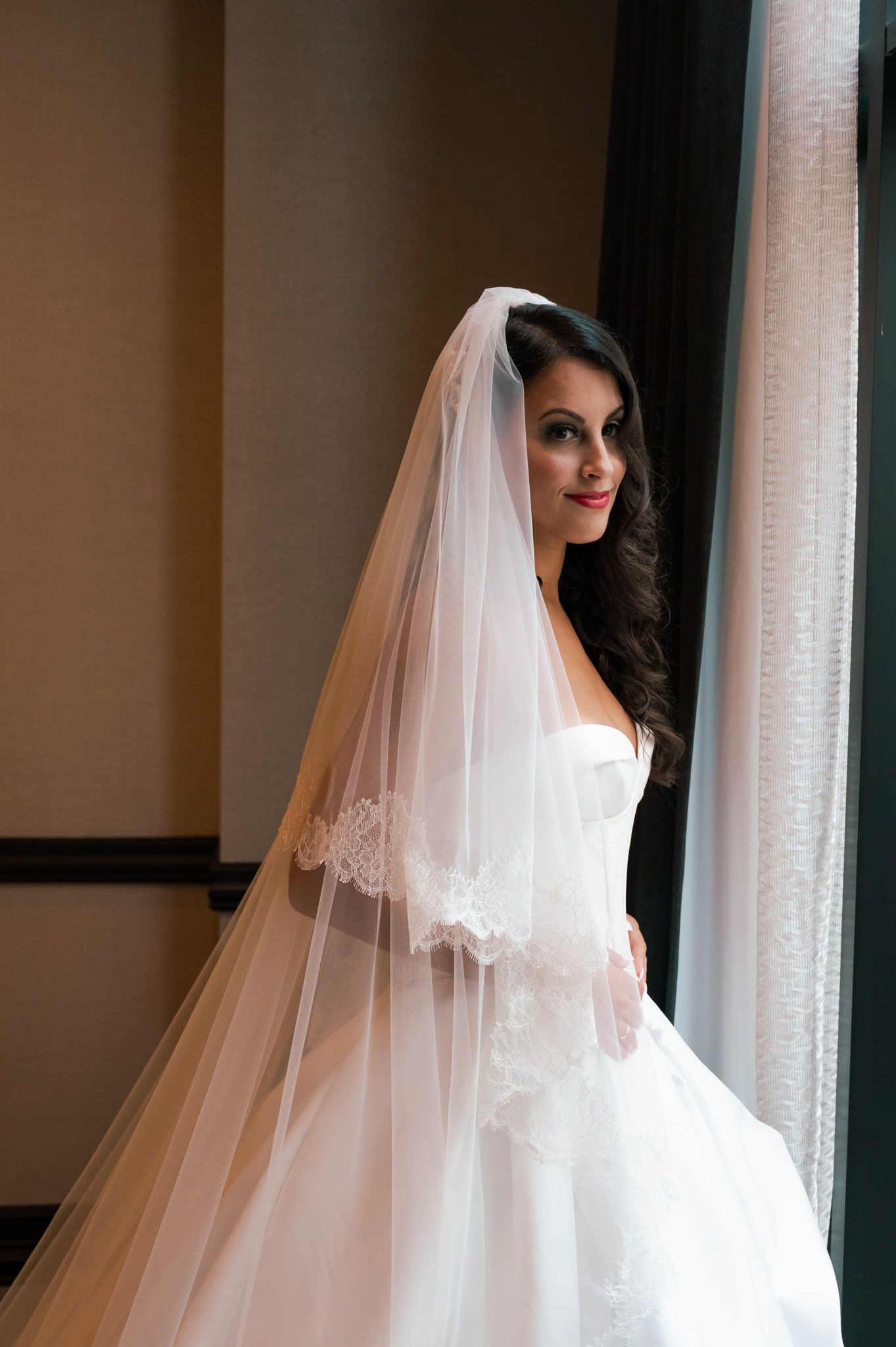 Elegant bridal portrait featuring delicate lace veil near window light.
