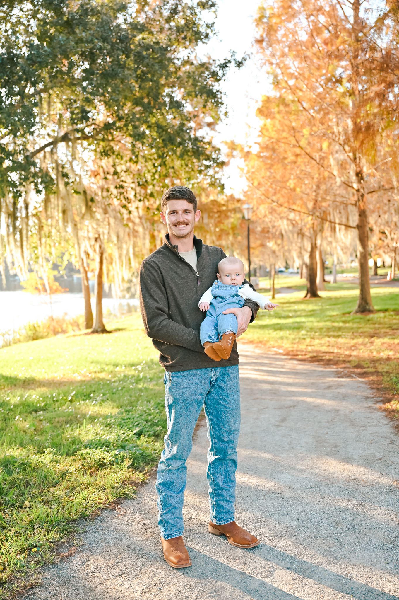 A family takes outdoor photos together on a scenic path with fall foliage.