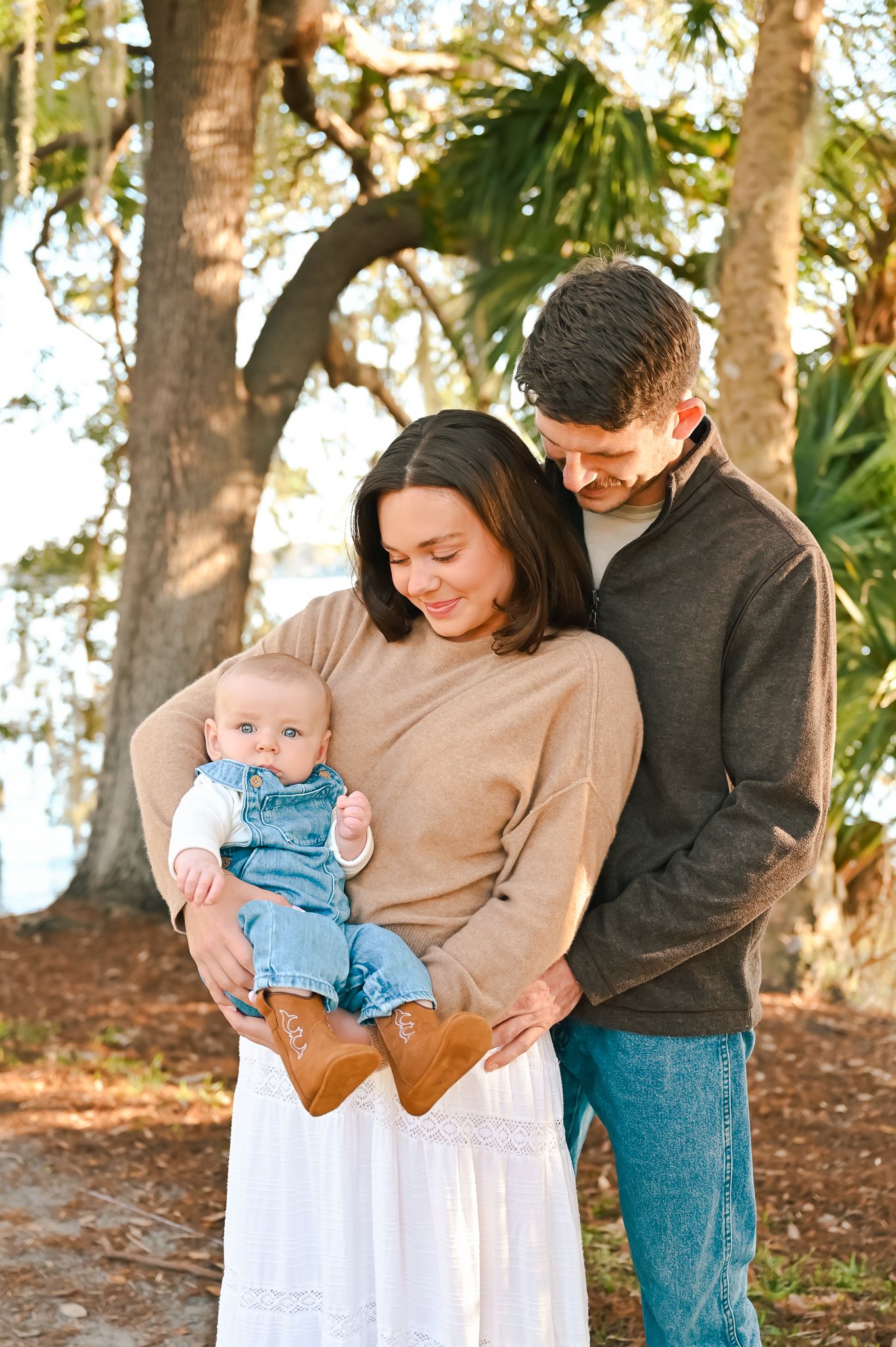 A family poses together outdoors in casual attire against a backdrop of trees.