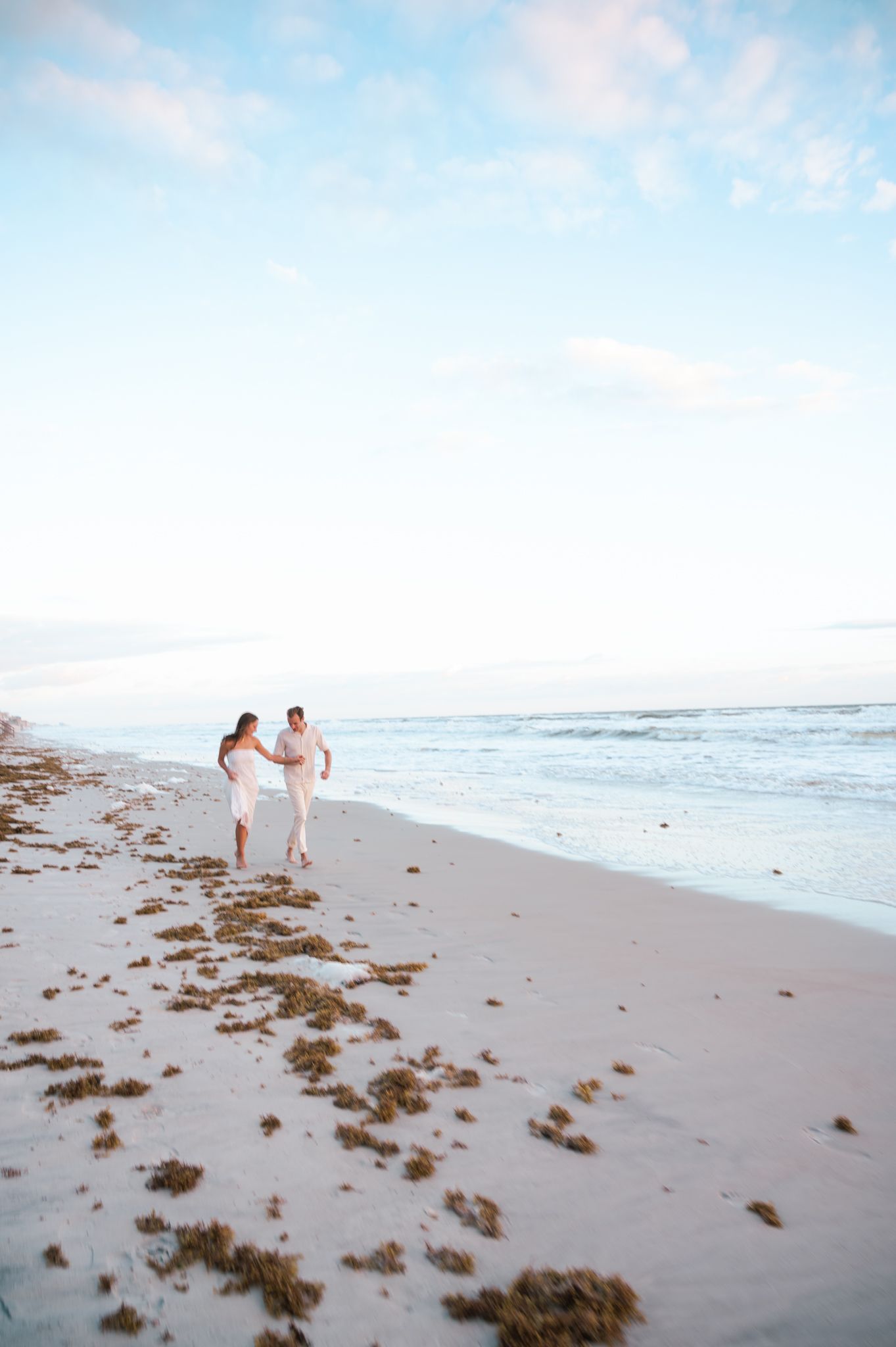 Couple walking together on beach shoreline during sunset.