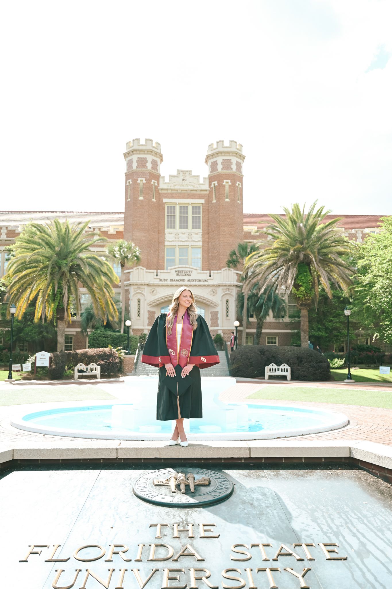 Florida State University graduate in cap and gown stands proudly at the iconic Westcott fountain on FSU campus.