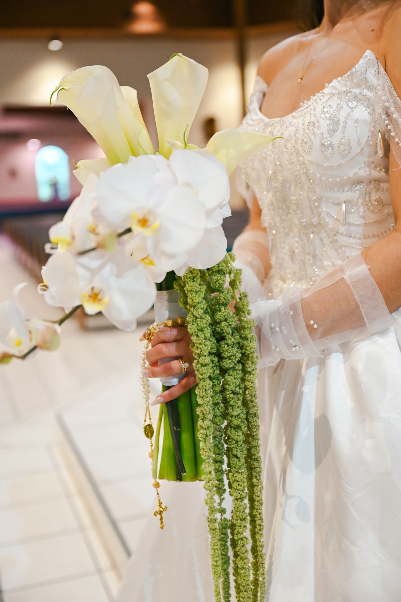 Elegant bridal bouquet featuring white orchids, calla lilies and cascading green amaranthus against a white wedding dress.