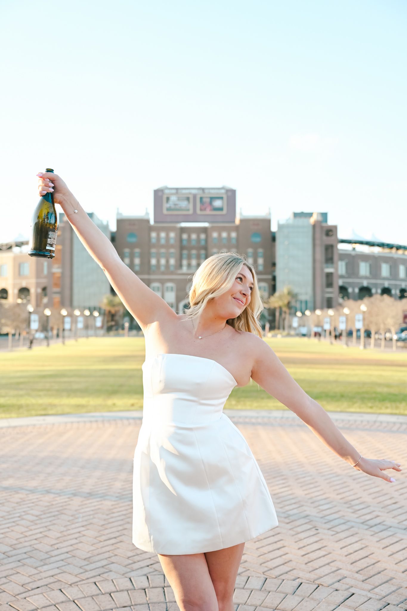 A person in a white dress twirls playfully on a brick paved plaza with urban buildings in the background.