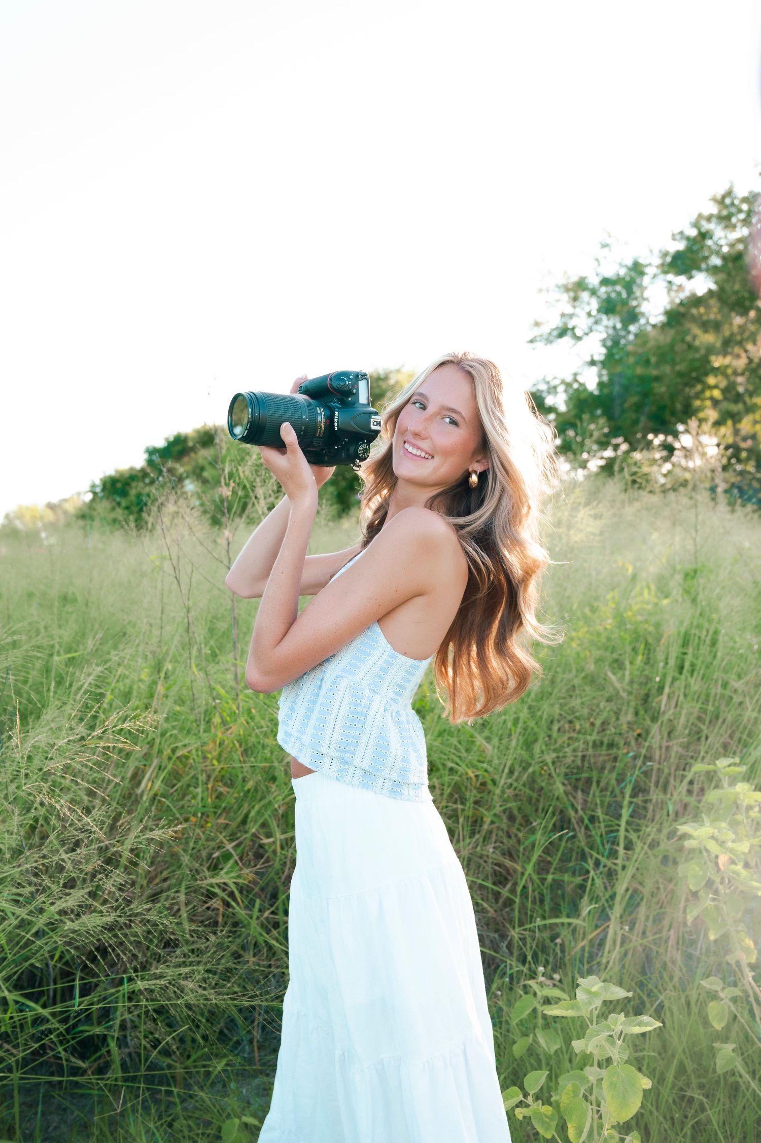 Photographer in light blue dress capturing photos outdoors in natural setting.