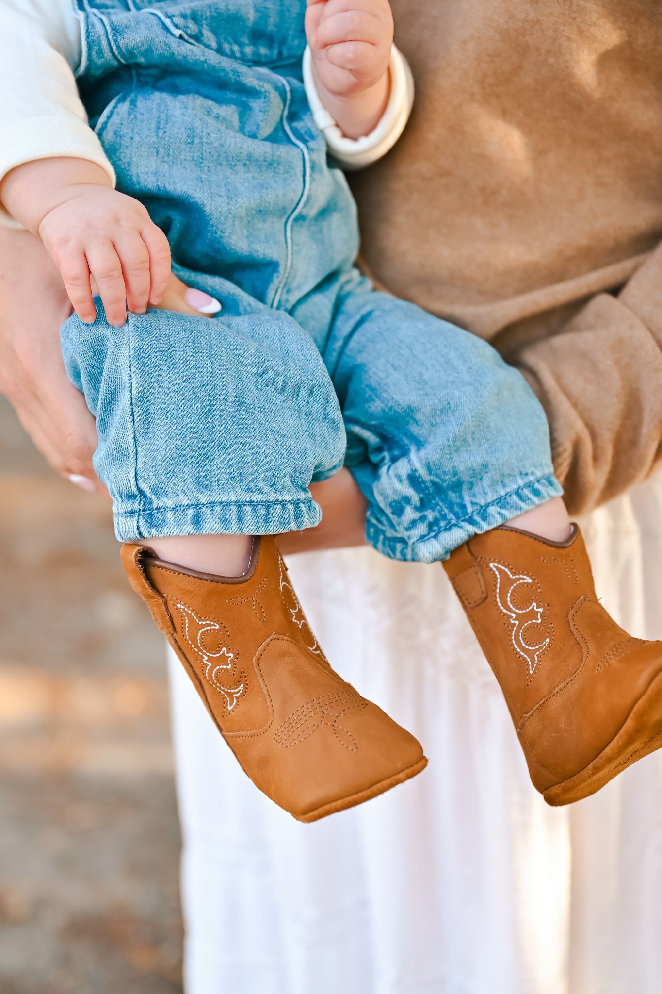 Close-up of tiny brown boots and denim overalls on a baby.