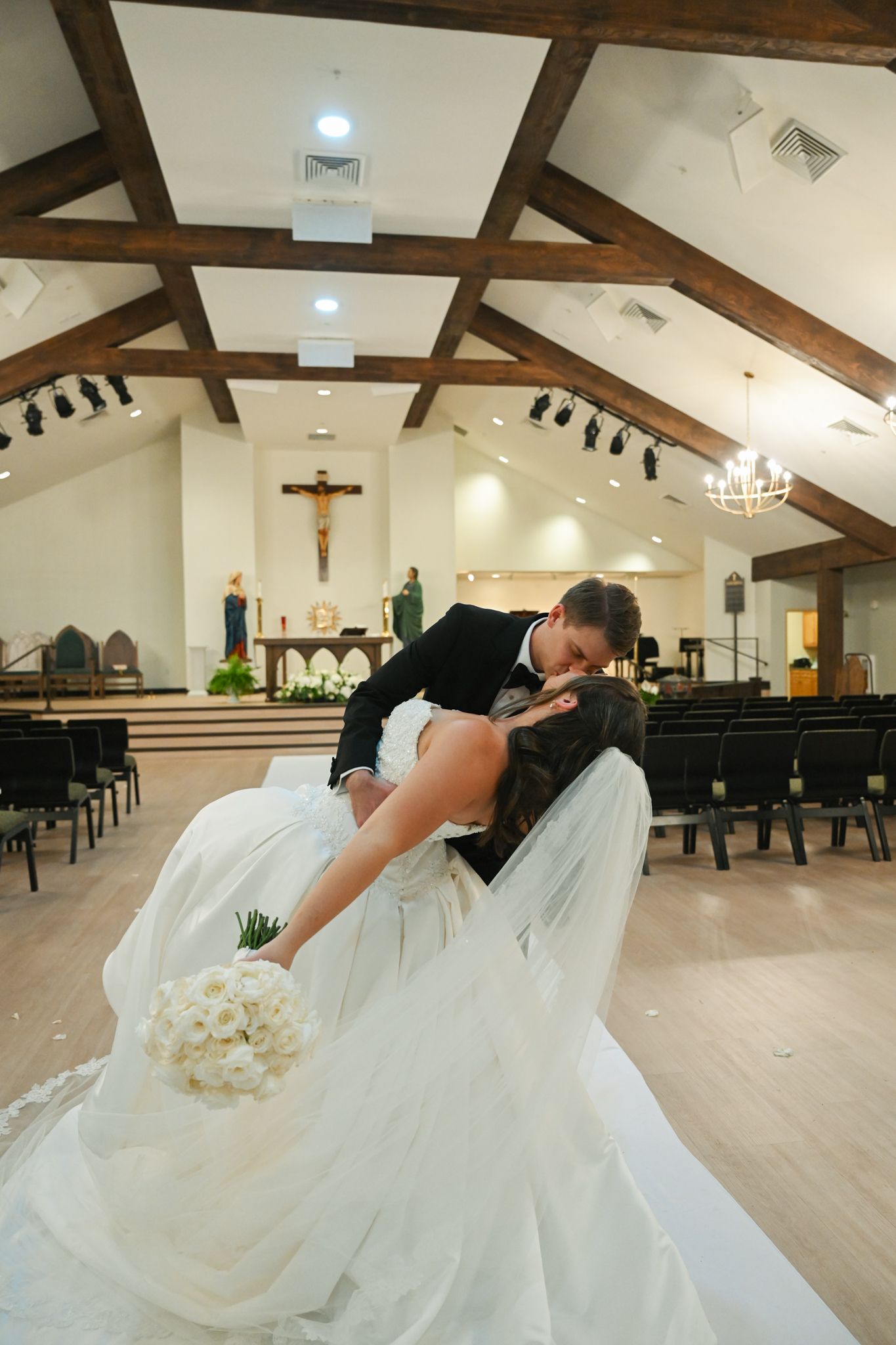 Bride and groom share a romantic dip kiss in a beautiful Catholic church after their wedding ceremony.