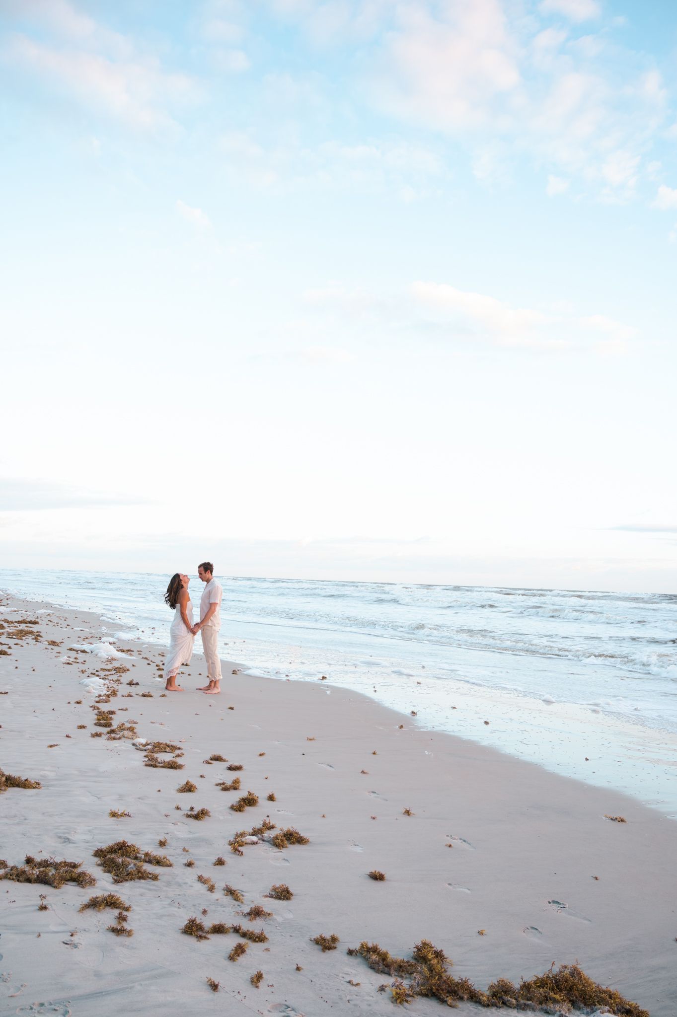Distant view of beachside wedding photography session on sandy shoreline.