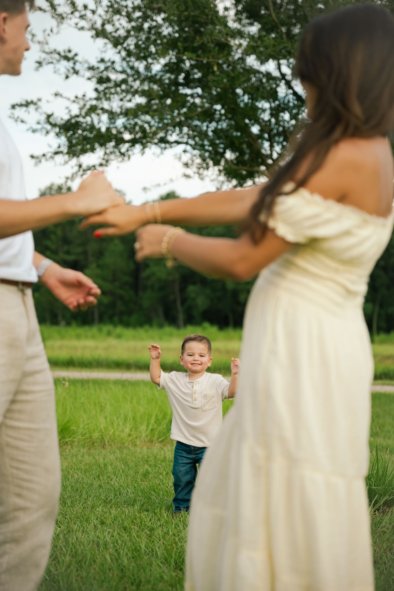 A joyful young boy runs toward his parents with arms outstretched in a lush green park setting.