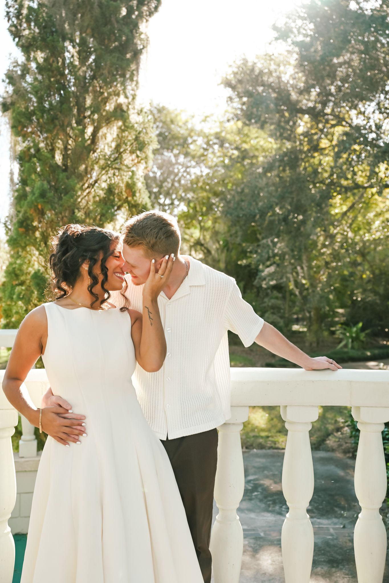Couple in white outfits sharing romantic kisses in sequence against a sunlit garden backdrop with white balustrade.